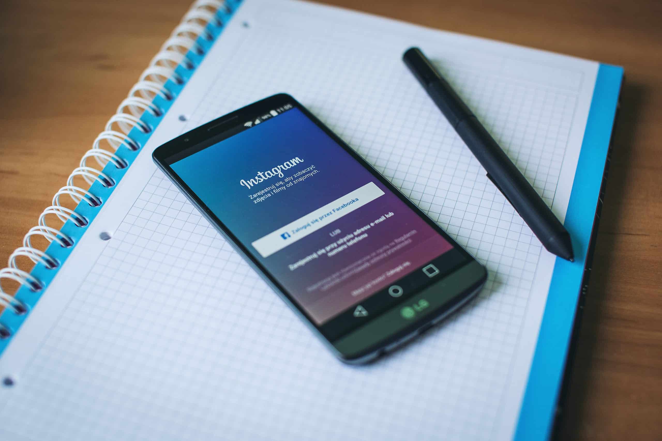 Facebook login page shown on a smartphone that is resting on a notebook and next to a pen