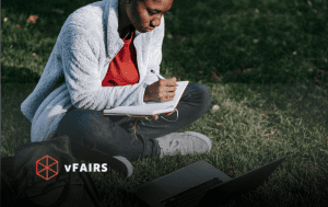 Student in a field with laptop and notebook